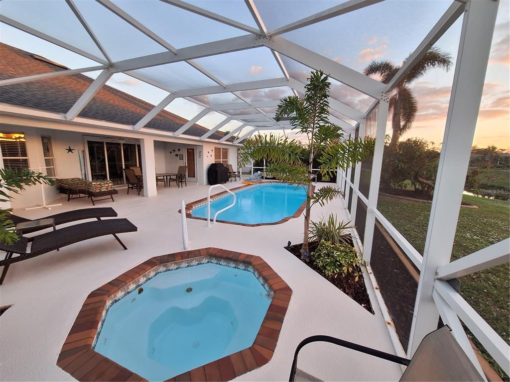 A screened-in patio features a swimming pool, a hot tub, and lounge chairs at sunset — 119 SPORTSMAN ROAD, ROTONDA WEST, FL