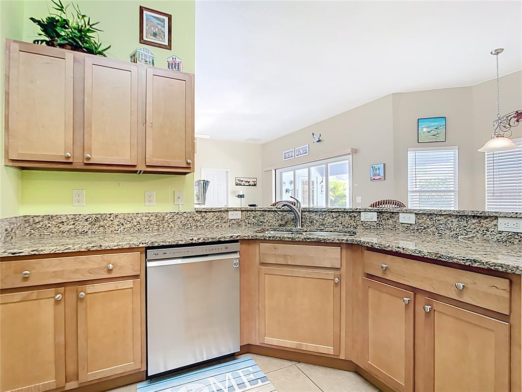 A kitchen features light wood cabinets, granite countertops, a stainless steel dishwasher, and tile flooring — 119 SPORTSMAN ROAD, ROTONDA WEST, FL