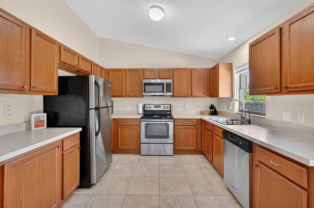 A kitchen features wood cabinets, stainless steel appliances, tile flooring, and light-colored countertops — 1520 3RD AVENUE, DELAND, FL