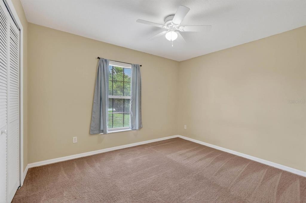 An empty bedroom features beige walls, brown carpet, a ceiling fan, and a window — 1520 3RD AVENUE, DELAND, FL