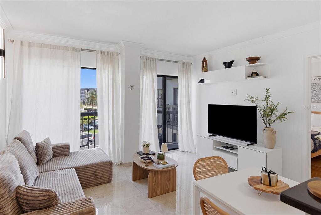 A bright living room features a sectional sofa, a television console, and two balcony doors — 6165 CARRIER DRIVE UNIT 1304, ORLANDO, FL