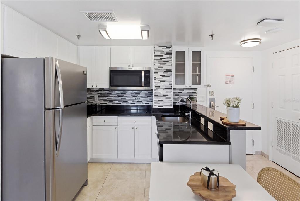 A kitchen with white cabinets, stainless steel appliances, black countertops, and a tiled backsplash — 6165 CARRIER DRIVE UNIT 1304, ORLANDO, FL