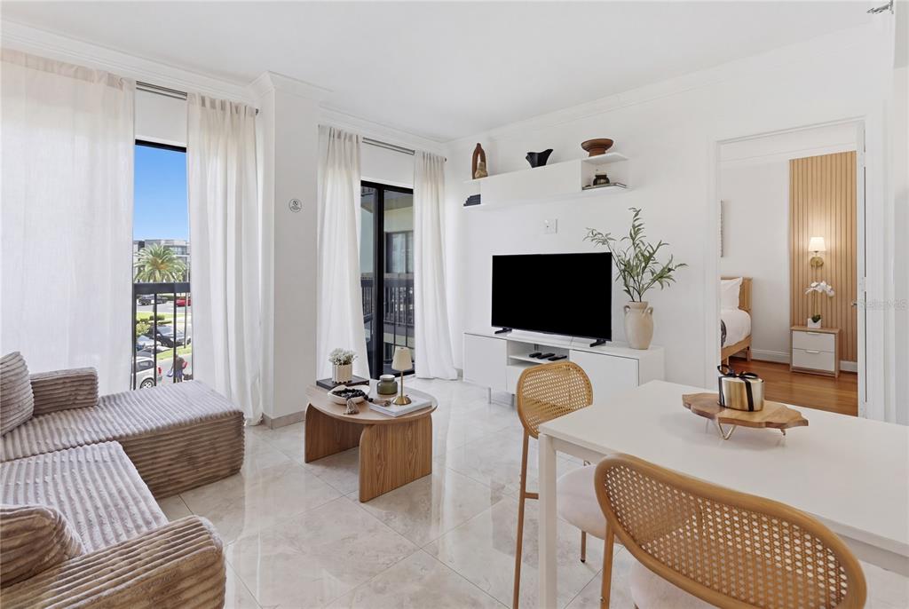 A bright living and dining area features white tile floors, a television console, and balcony access — 6165 CARRIER DRIVE UNIT 1304, ORLANDO, FL