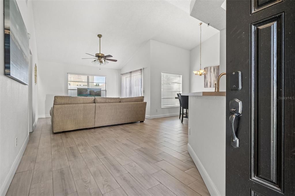 A living room with light wood-look flooring, a beige sectional sofa, and a ceiling fan — 12714 TROWBRIDGE LANE, TAMPA, FL