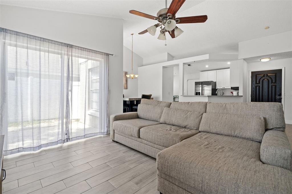 A living room features a gray sectional sofa, light wood-look tile floors, and a ceiling fan — 12714 TROWBRIDGE LANE, TAMPA, FL