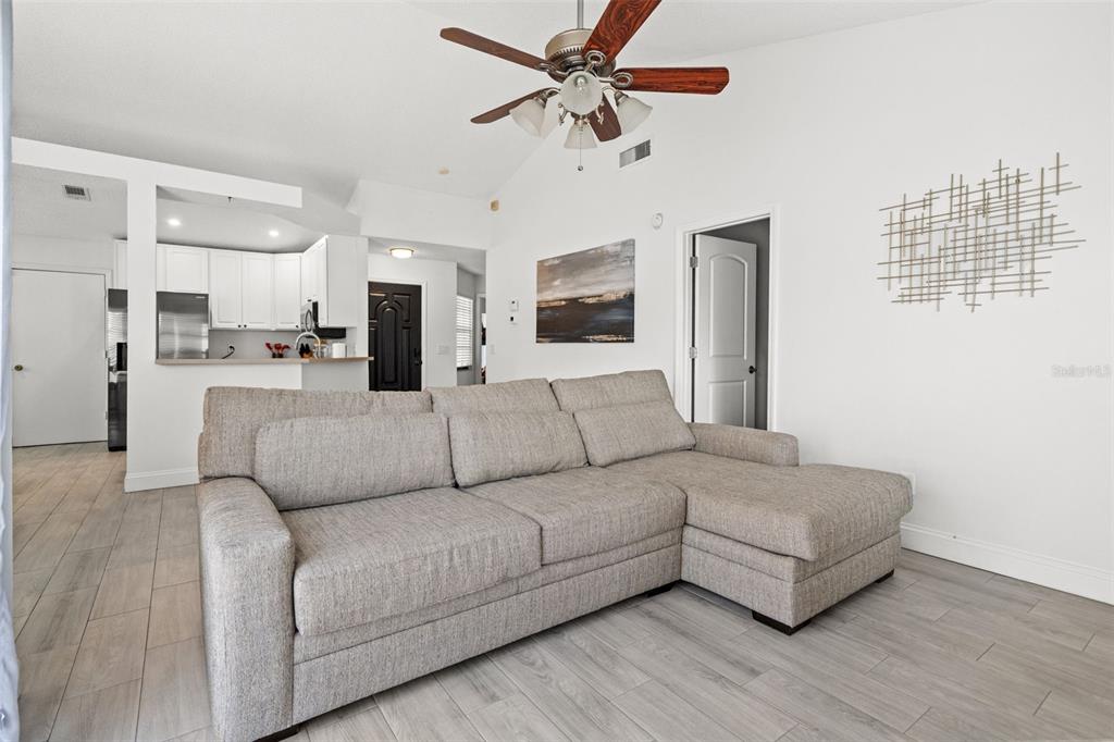 A living room features a gray sectional sofa, light wood-look flooring, and a ceiling fan — 12714 TROWBRIDGE LANE, TAMPA, FL