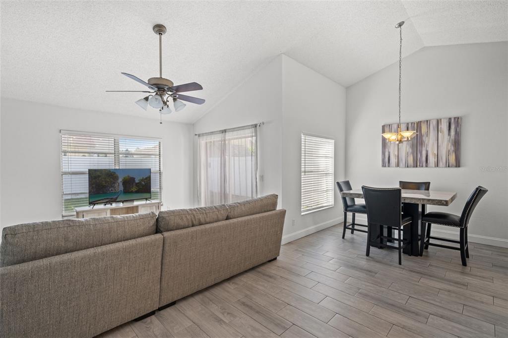 A living and dining area with vaulted ceilings, gray wood-look flooring, and a ceiling fan — 12714 TROWBRIDGE LANE, TAMPA, FL