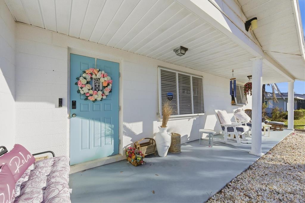 A covered front porch features a light blue door, white siding, and outdoor seating — 1710 FLORENCE AVENUE, ENGLEWOOD, FL