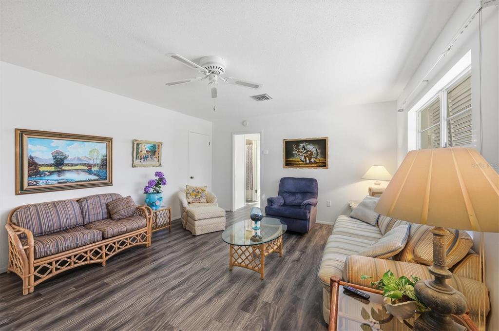 A living room features wood-look flooring, a ceiling fan, and various seating options — 1710 FLORENCE AVENUE, ENGLEWOOD, FL