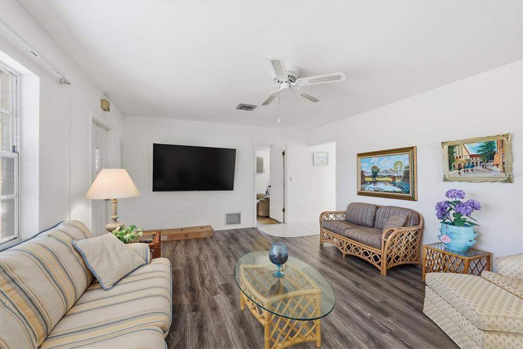 A living room features wood-look flooring, a ceiling fan, a wall-mounted television, and wicker furniture — 1710 FLORENCE AVENUE, ENGLEWOOD, FL