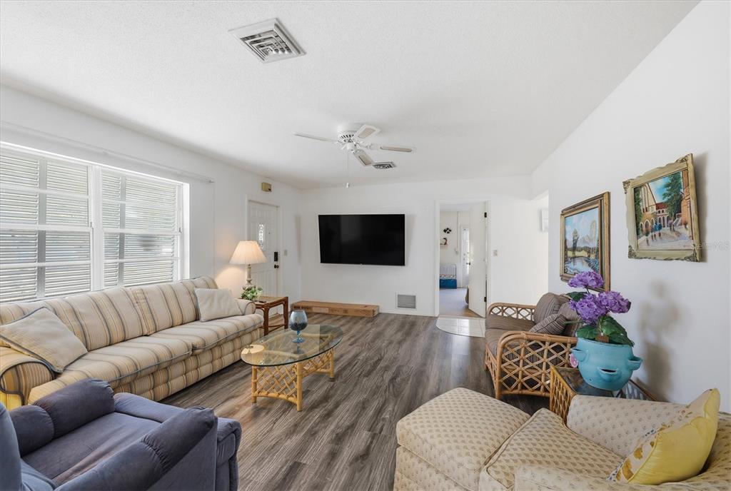 A living room features wood-look flooring, a striped sofa, a television, and wicker furniture — 1710 FLORENCE AVENUE, ENGLEWOOD, FL
