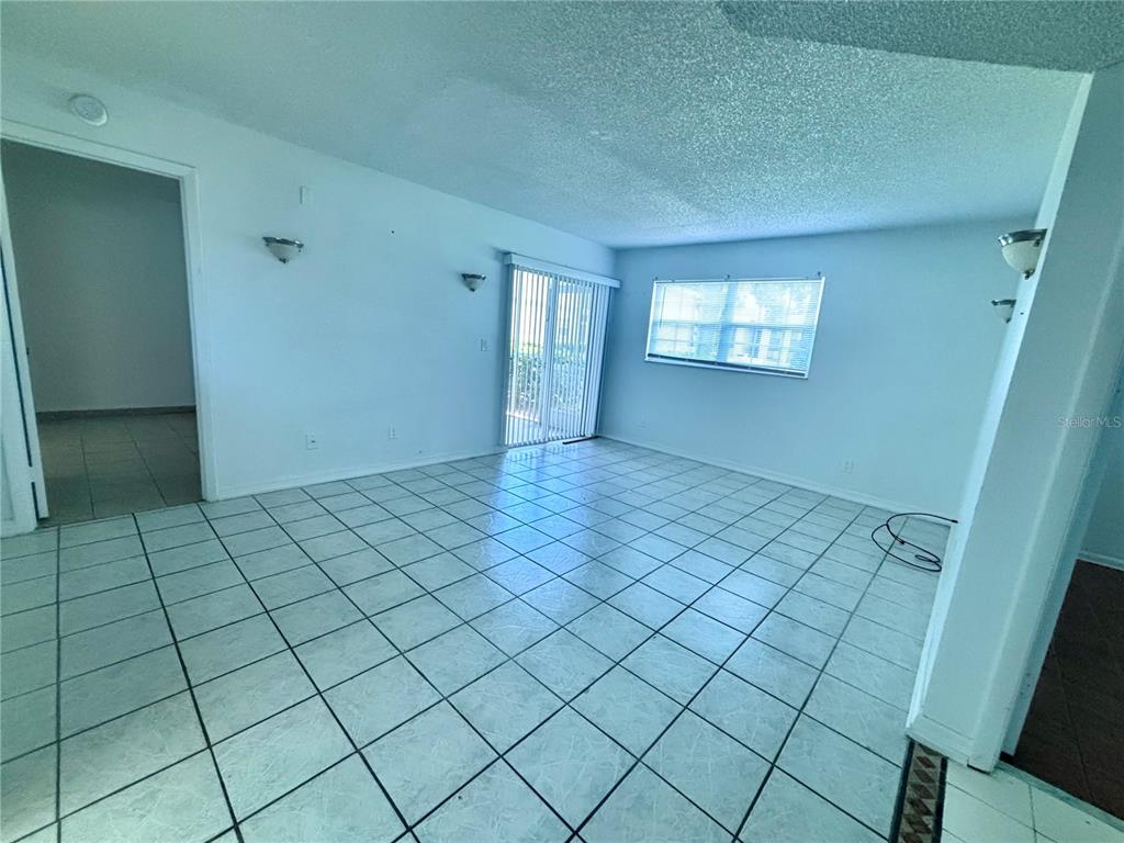 An empty room features light blue walls, white tiled flooring, and a sliding glass door — 576 FAIRWAYS LANE UNIT M104, OCALA, FL