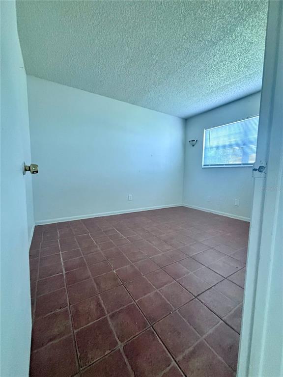 An empty room with white walls, a textured ceiling, and reddish-brown square floor tiles — 576 FAIRWAYS LANE UNIT M104, OCALA, FL