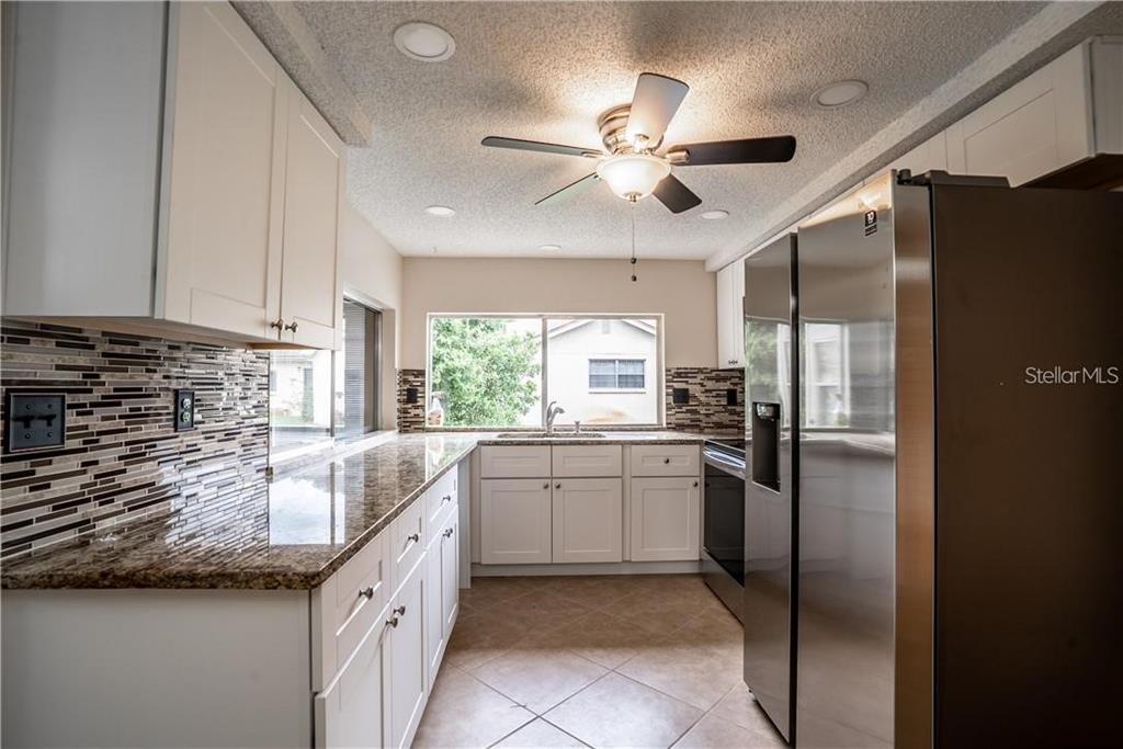 A kitchen with white cabinets, granite countertops, a mosaic tile backsplash, and stainless steel appliances — 12217 BUTTONWOOD ROW, HUDSON, FL