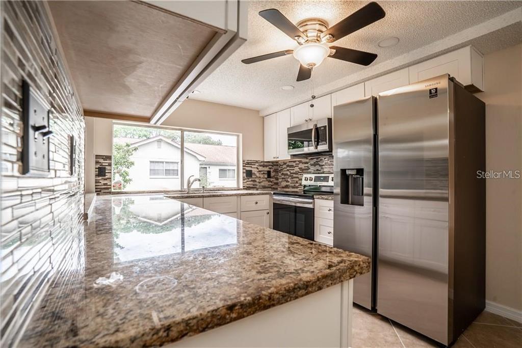 A kitchen features granite countertops, stainless steel appliances, white cabinetry, and a tiled backsplash — 12217 BUTTONWOOD ROW, HUDSON, FL