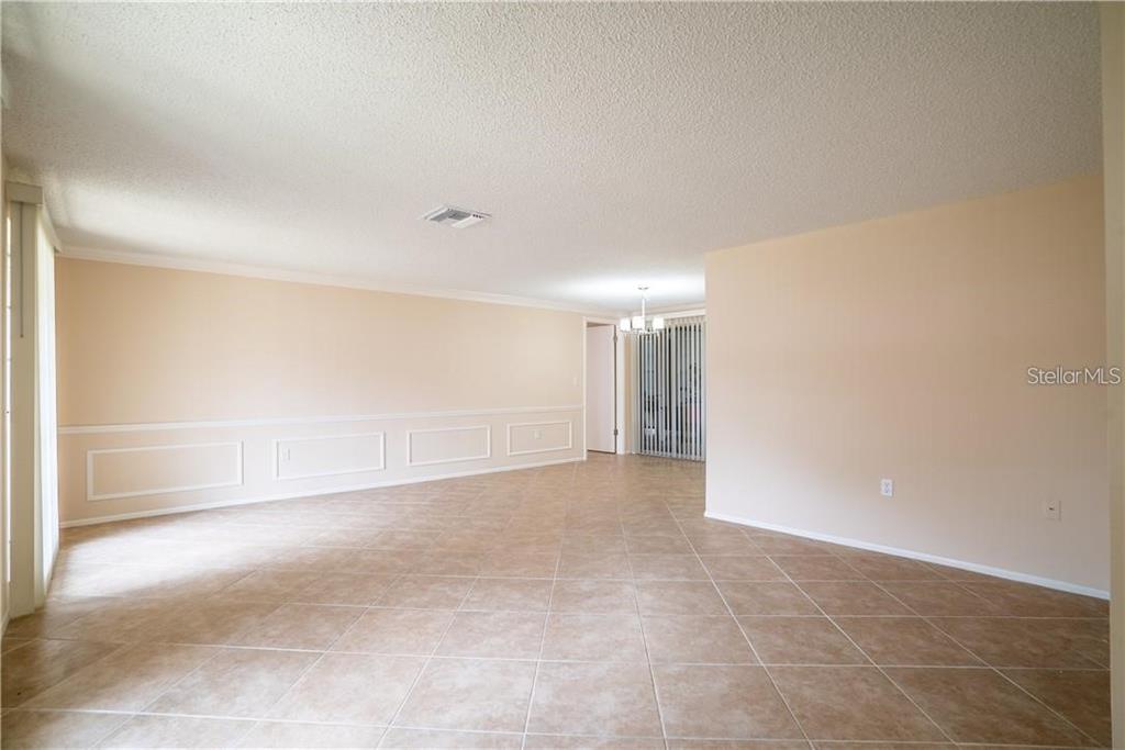 An empty room with beige walls, wainscoting, and light-colored tile flooring — 12217 BUTTONWOOD ROW, HUDSON, FL