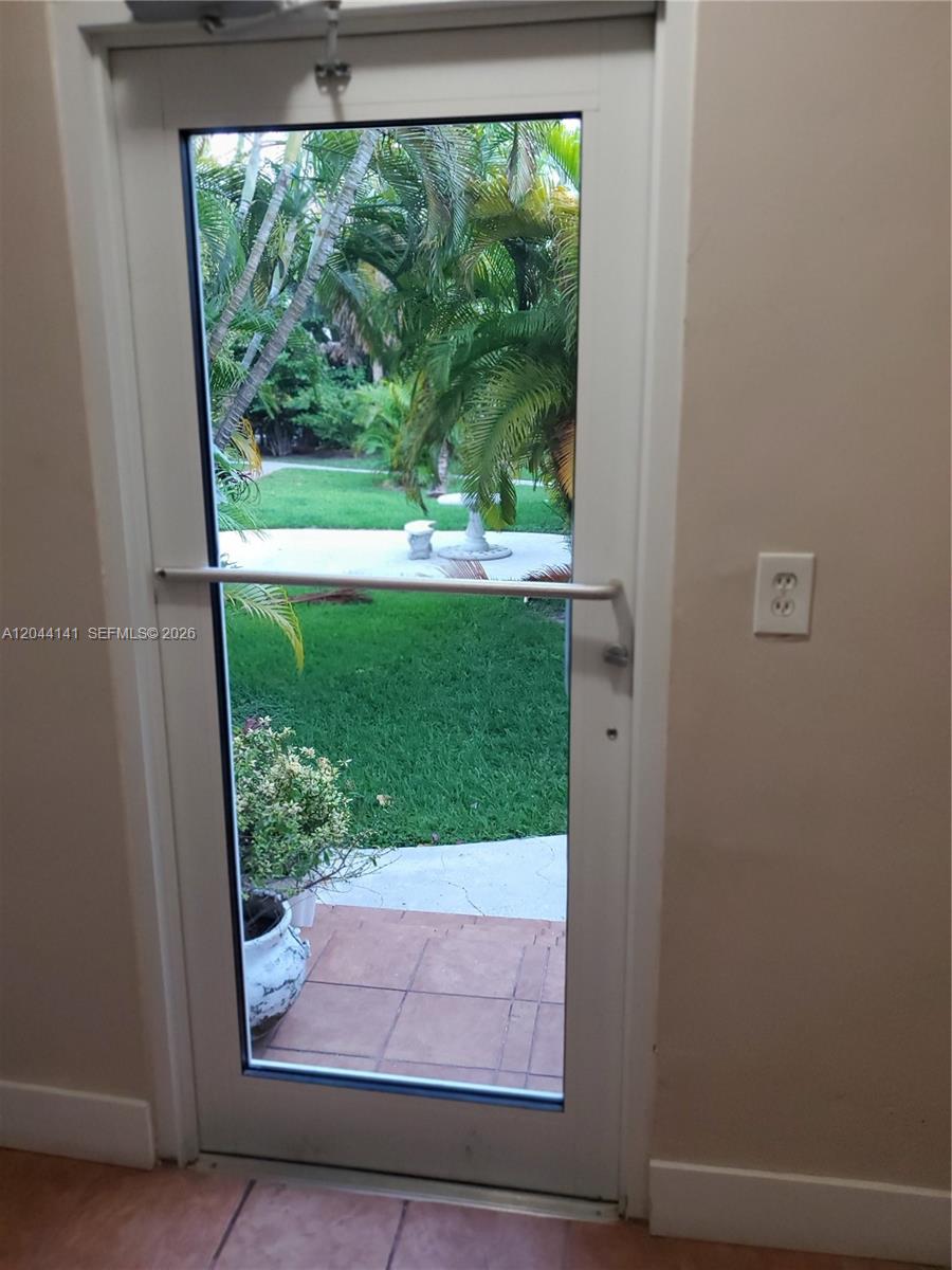 A glass-paneled door with a horizontal security bar opens to a backyard with palm trees — 10074 E Bay Harbor Dr # 74A, Bay Harbor Islands FL 33154, BAY HARBOR ISLANDS, FL