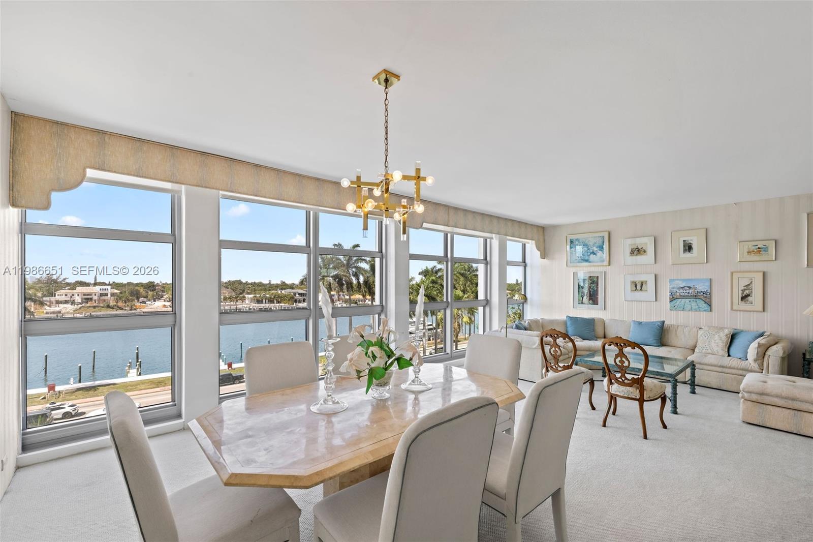A dining and living area features a stone table, chandelier, and floor-to-ceiling waterfront windows — 5055 Collins Ave # 5M, Miami Beach FL 33140, MIAMI BEACH, FL