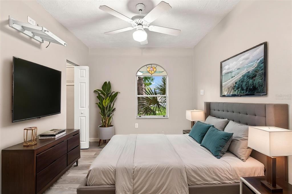 A bedroom features a bed with a gray headboard, a ceiling fan, and a wall-mounted television — 1005 ALSTON LANE, ENGLEWOOD, FL