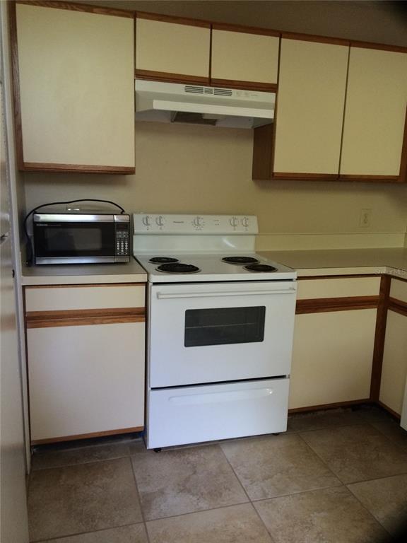 A kitchen features white cabinets with wood trim, a white electric stove, and tile flooring — 625 GREENCOVE TERRACE UNIT 120, ALTAMONTE SPRINGS, FL