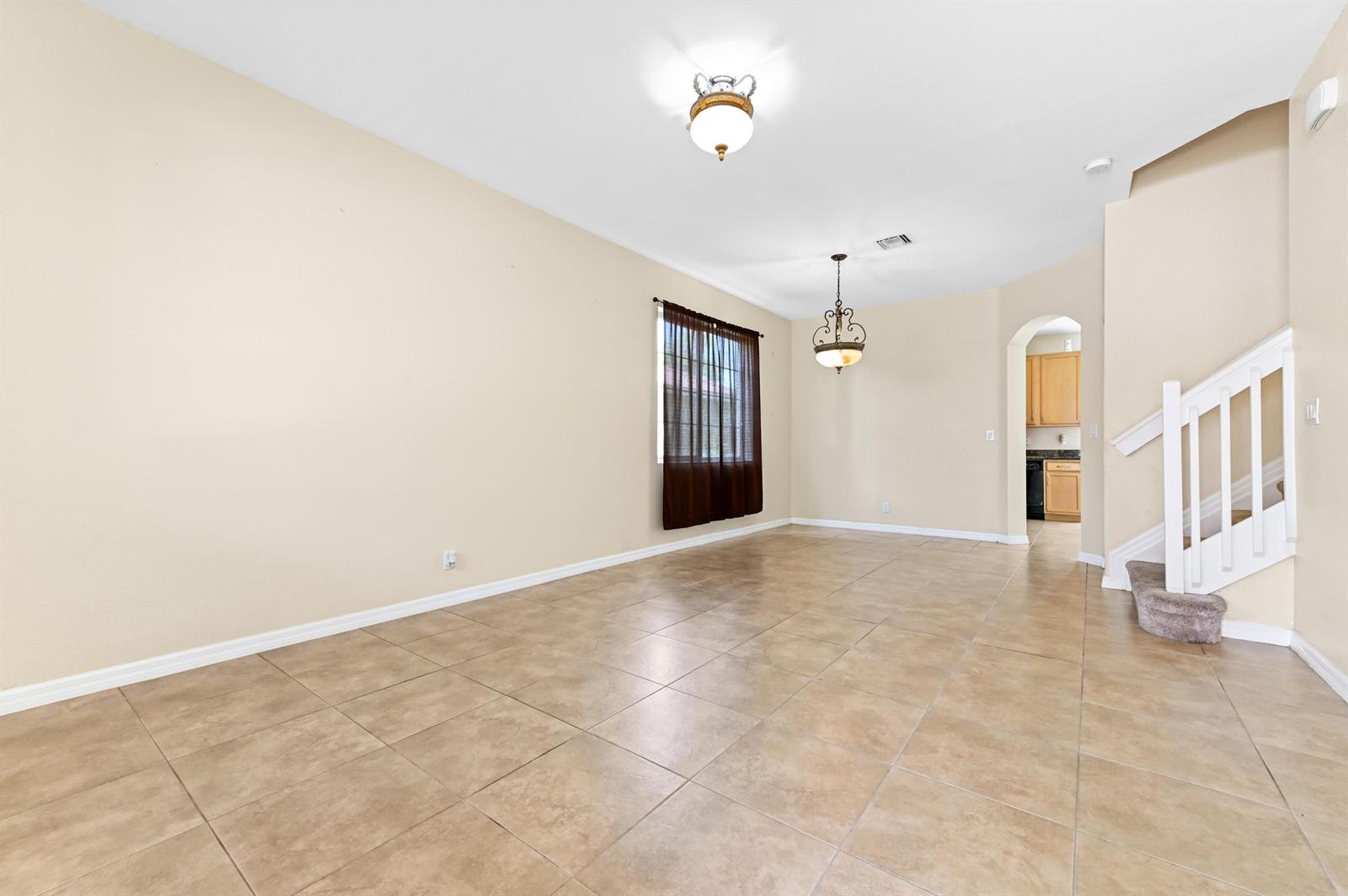 An empty room with beige walls, tile flooring, a window with curtains, and a staircase — 6819 Osage Circle, West Palm Beach FL 33413, WEST PALM BEACH, FL