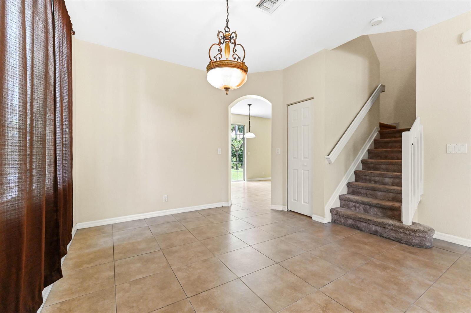 A tiled dining area features a chandelier, a staircase, and an arched doorway to another room — 6819 Osage Circle, West Palm Beach FL 33413, WEST PALM BEACH, FL