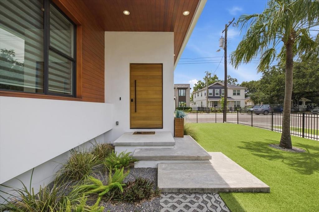 A modern home entrance features a wood door, concrete steps, and a landscaped front yard — 2701 N POPLAR AVENUE, TAMPA, FL