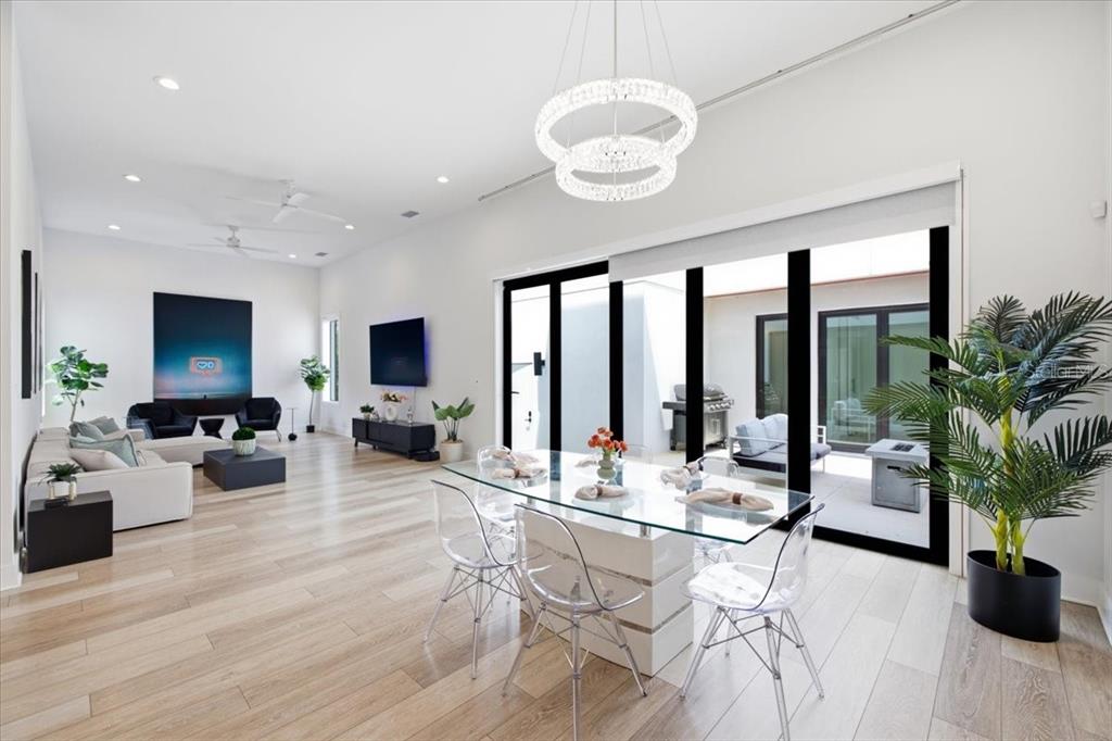 A modern open-concept living and dining area features light wood floors, a crystal chandelier, and sliding glass doors — 2701 N POPLAR AVENUE, TAMPA, FL