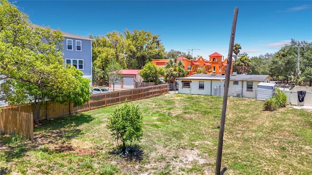 A grassy backyard features a wooden fence, a small tree, and neighboring residential buildings — 2304 N HIGHLAND AVENUE, TAMPA, FL
