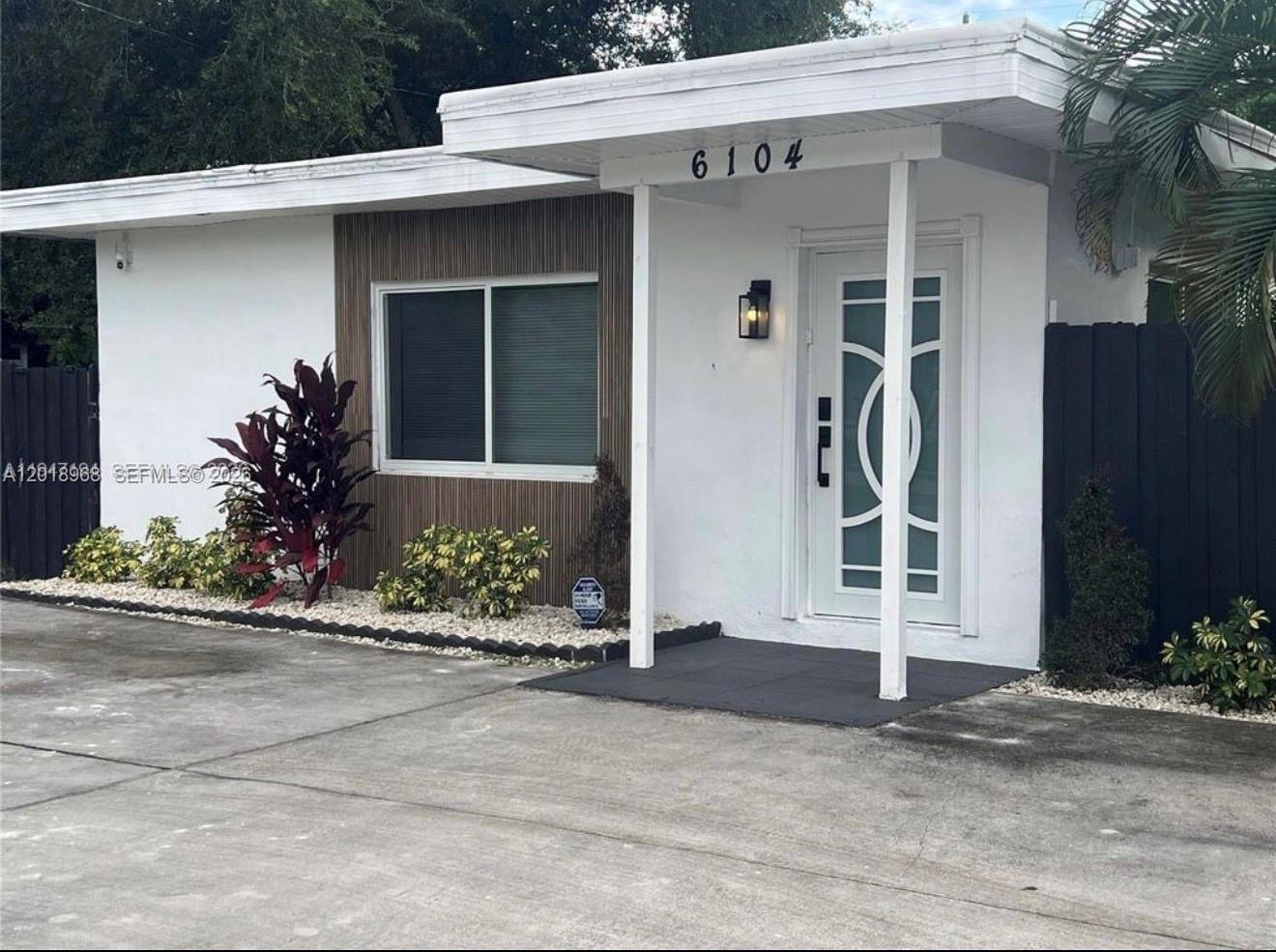 The exterior of a white house features a modern front door and wood-slat accent wall — 6104 SW 33rd St, Miramar FL 33023, MIRAMAR, FL