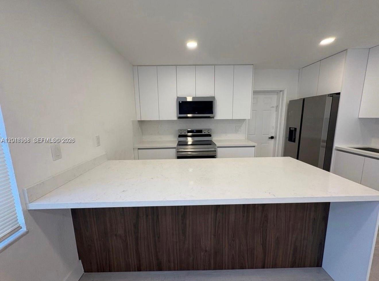 A kitchen features white cabinets, stainless steel appliances, and a large white quartz island — 6104 SW 33rd St, Miramar FL 33023, MIRAMAR, FL