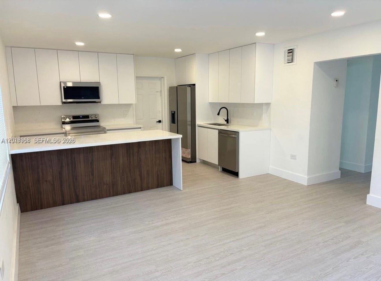 A modern kitchen features white cabinetry, stainless steel appliances, and a wood-paneled peninsula island — 6104 SW 33rd St, Miramar FL 33023, MIRAMAR, FL