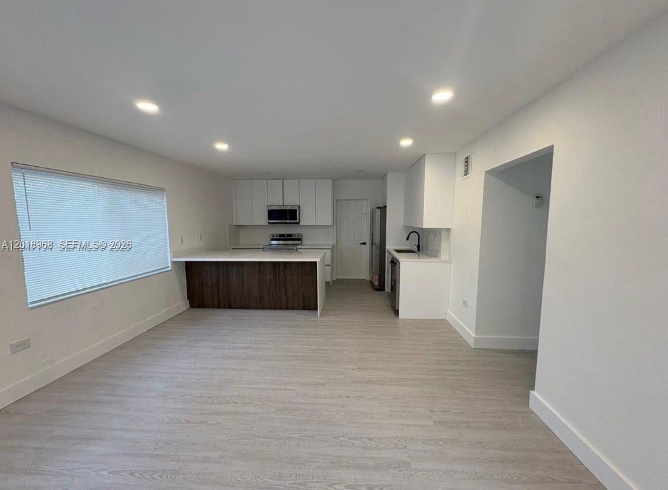A modern kitchen features white cabinets, a dark wood island, and light-colored flooring — 6104 SW 33rd St, Miramar FL 33023, MIRAMAR, FL