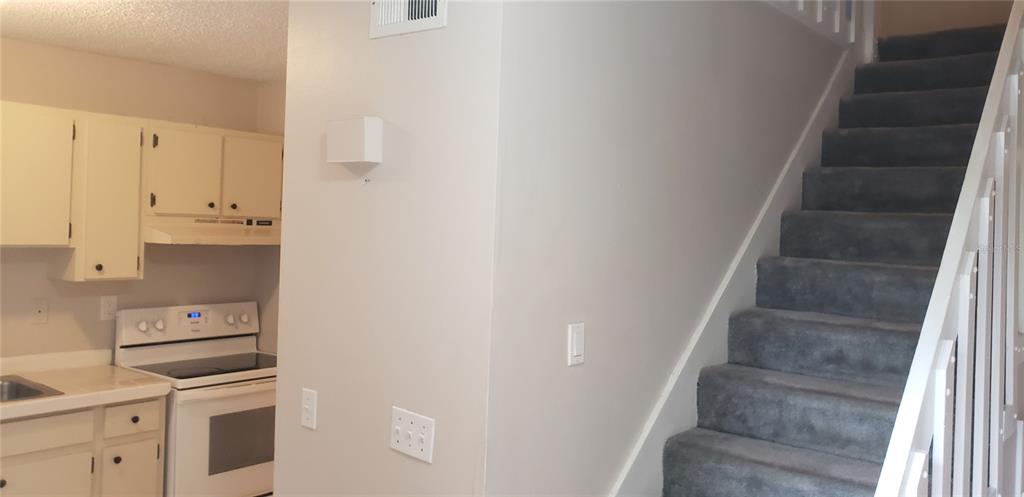 A kitchen with white cabinets and a stove sits beside a carpeted staircase — 22726 GAGE LOOP UNIT 41, LAND O LAKES, FL