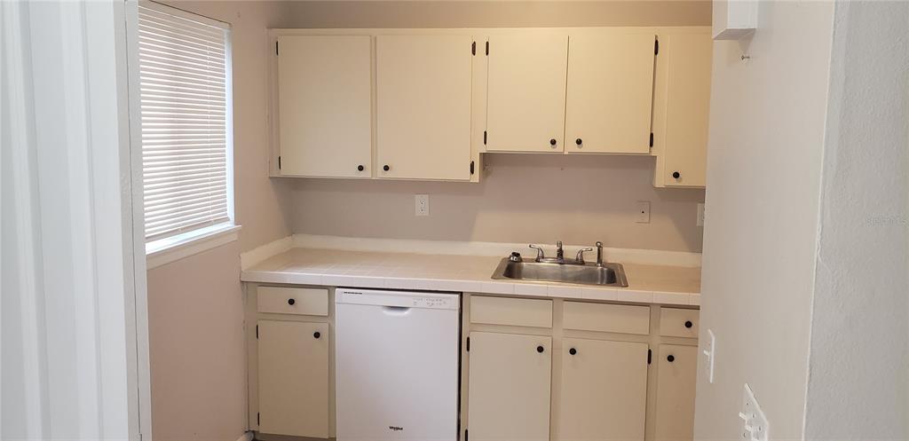 A kitchen features off-white cabinets, tiled countertops, a stainless steel sink, and a white dishwasher — 22726 GAGE LOOP UNIT 41, LAND O LAKES, FL