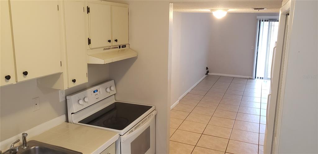 A kitchen with white cabinets and appliances opens into a tiled dining area with sliding doors — 22726 GAGE LOOP UNIT 41, LAND O LAKES, FL