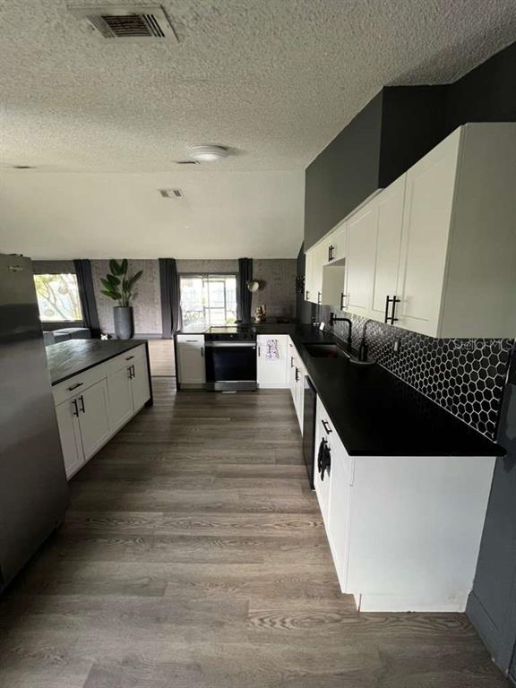 A kitchen features white cabinets, black countertops, a hexagonal tile backsplash, and wood-look flooring — 906 SAN PAULO WAY, KISSIMMEE, FL