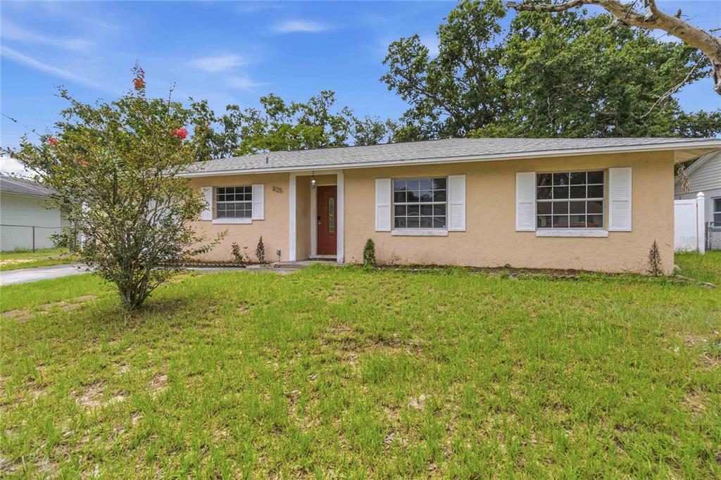 A single-story house with tan stucco siding, white shutters, and a red front door — 825 TURTLE MOUND DRIVE, CASSELBERRY, FL