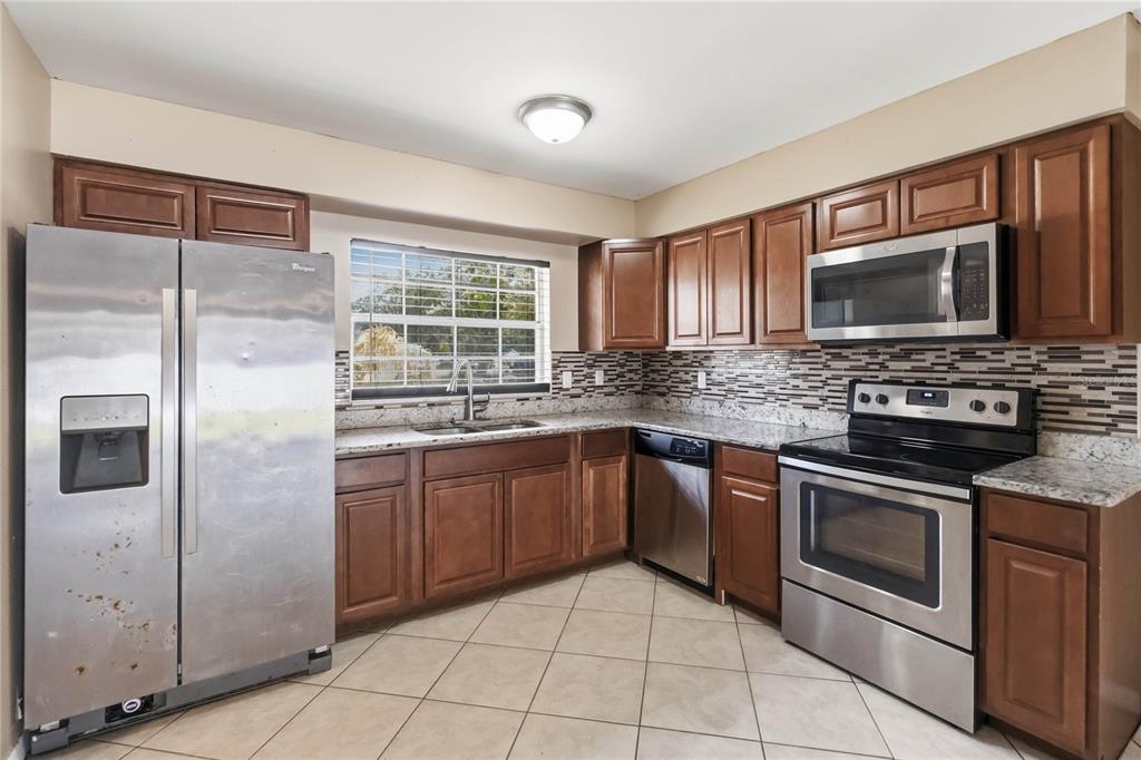 A kitchen featuring wood cabinets, stainless steel appliances, granite countertops, and a tiled floor — 825 TURTLE MOUND DRIVE, CASSELBERRY, FL