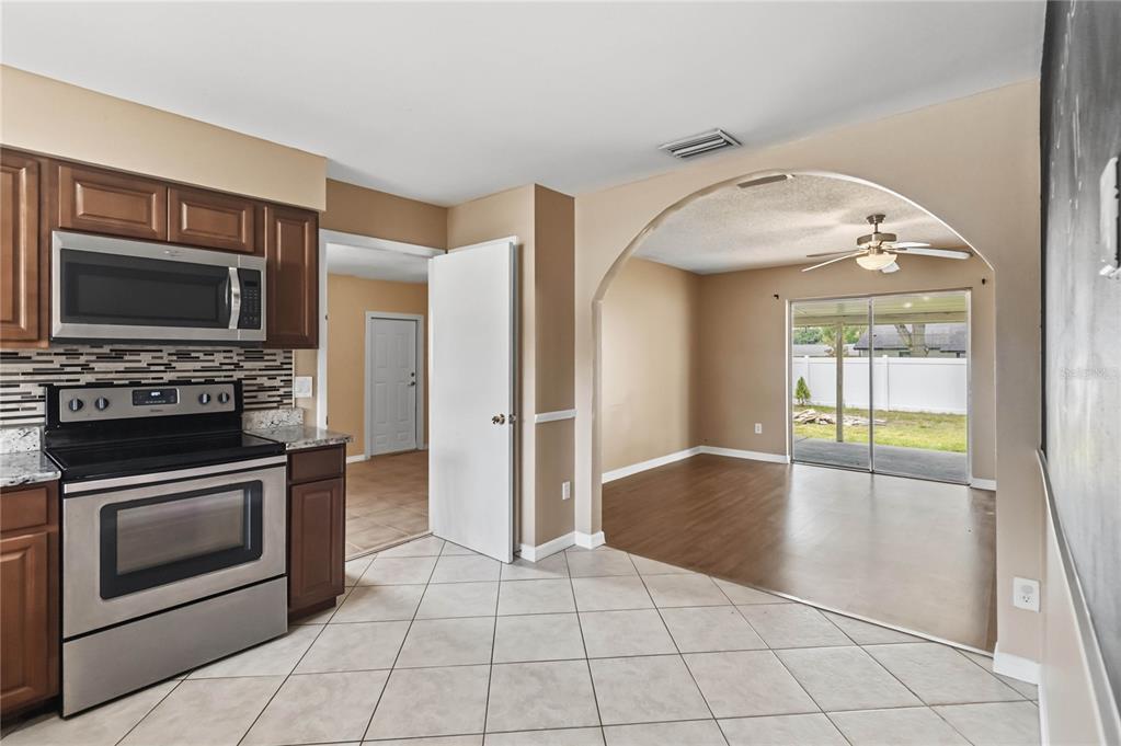 A kitchen with tile floors and stainless steel appliances opens into a living area — 825 TURTLE MOUND DRIVE, CASSELBERRY, FL