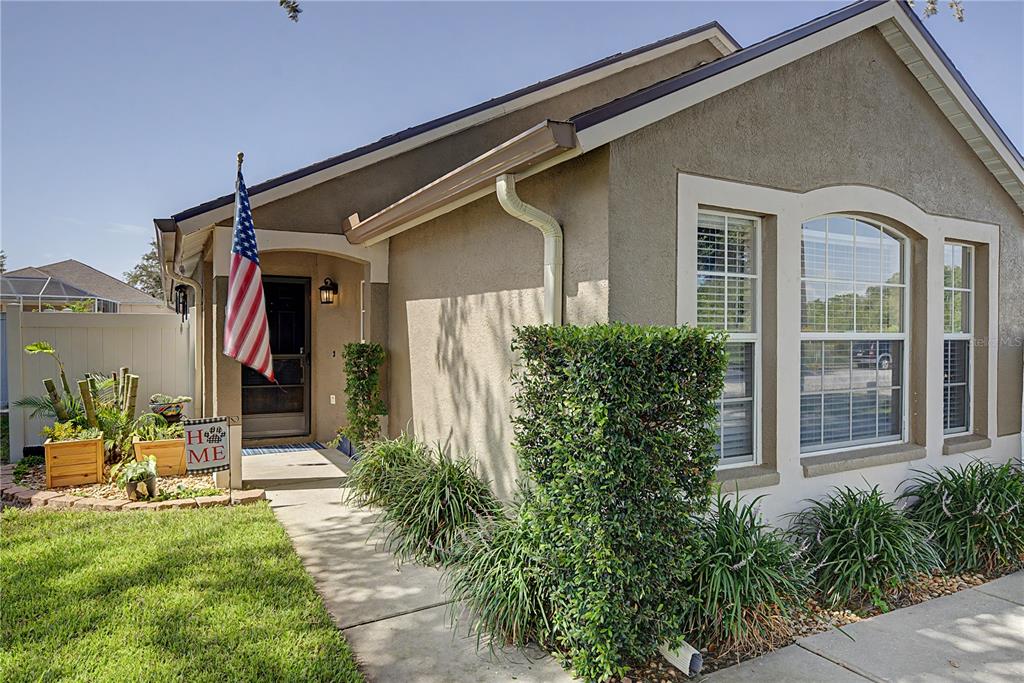 A tan stucco house with a front porch, an American flag, and landscaped garden beds — 24328 MISTWOOD COURT, LUTZ, FL