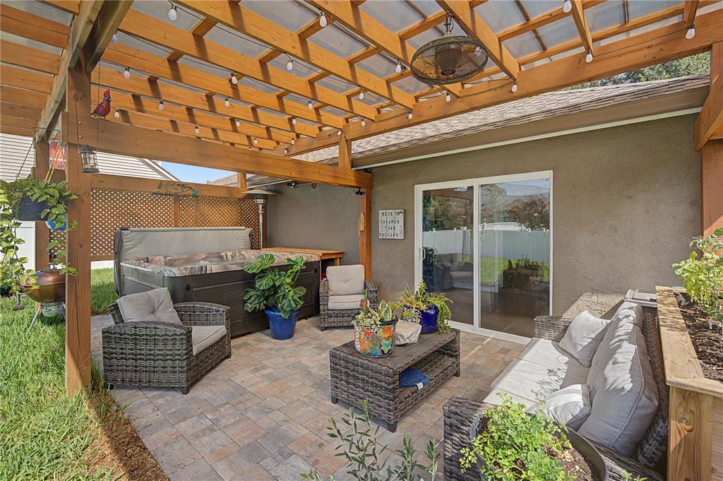 A covered patio features a hot tub, wicker furniture, and a wooden pergola with string lights — 24328 MISTWOOD COURT, LUTZ, FL