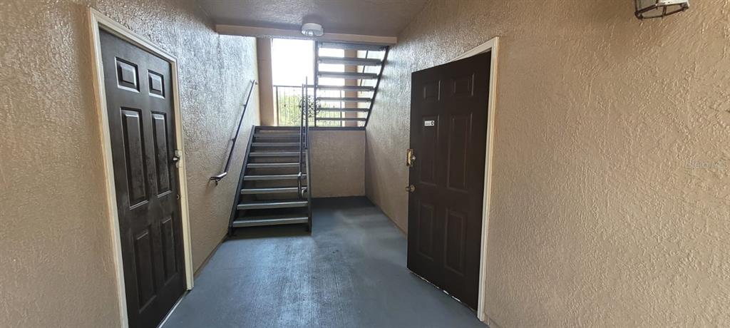 An outdoor apartment hallway features two dark brown doors, a staircase, and textured beige walls — 14328 FREDRICKSBURG DRIVE UNIT 601, ORLANDO, FL