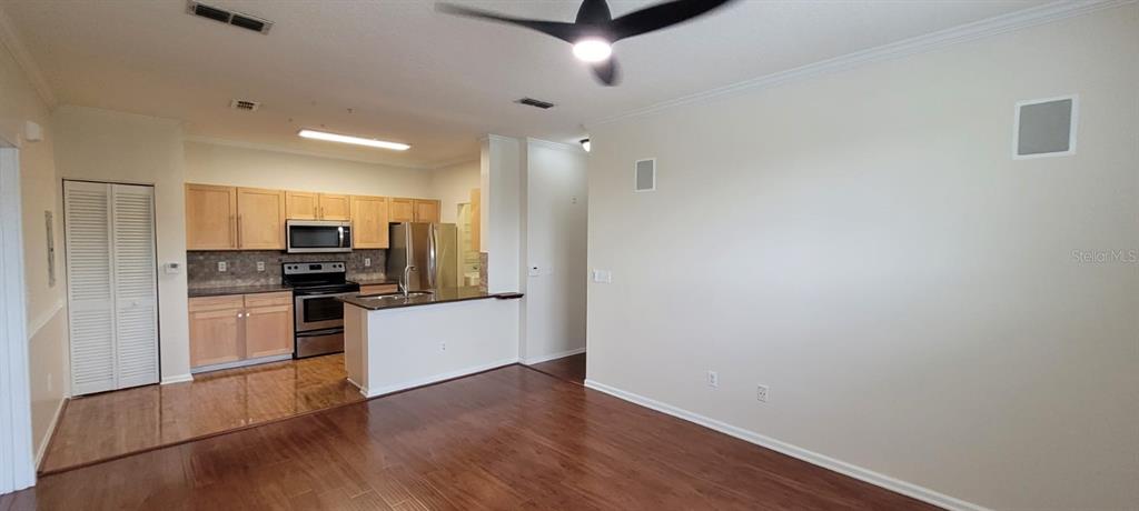 This open-concept kitchen features light wood cabinets, stainless steel appliances, and dark hardwood flooring — 14328 FREDRICKSBURG DRIVE UNIT 601, ORLANDO, FL