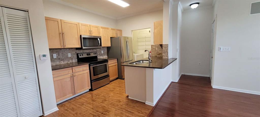 A kitchen features light wood cabinets, stainless steel appliances, and a dark countertop island — 14328 FREDRICKSBURG DRIVE UNIT 601, ORLANDO, FL