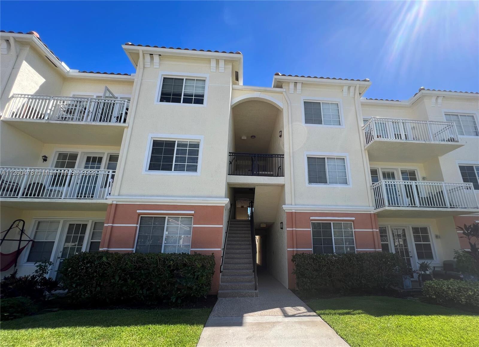 A three-story apartment building features beige stucco walls, white railings, and a central staircase — 9887 Baywinds Drive # 4305, West Palm Beach FL 33411, WEST PALM BEACH, FL