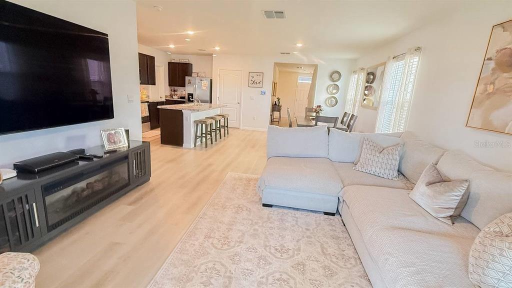 A living room with a large sectional sofa, light wood flooring, and an open kitchen — 1724 POST OAK DRIVE, DAVENPORT, FL