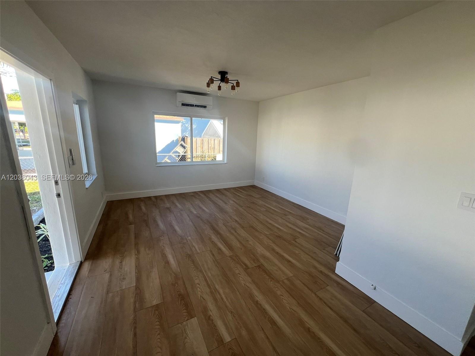 An empty room features wood-look flooring, white walls, a ceiling light, and a wall-mounted air conditioner — 1706 Arthur St, Hollywood FL 33020, HOLLYWOOD, FL