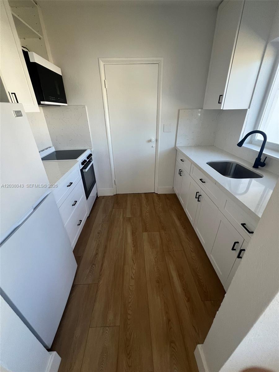 A galley kitchen features white cabinets, quartz countertops, stainless steel appliances, and wood-look flooring — 1706 Arthur St, Hollywood FL 33020, HOLLYWOOD, FL