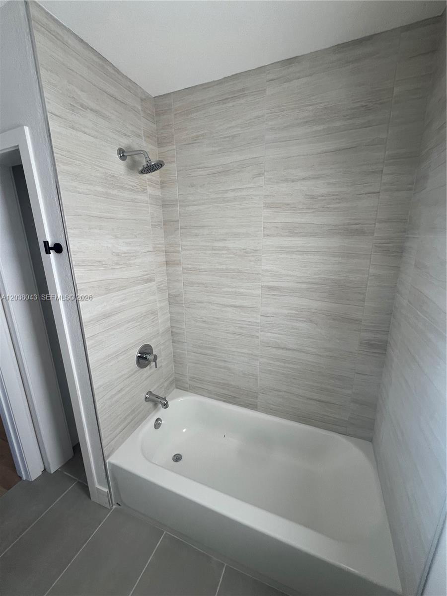 A bathroom features a white bathtub with a showerhead and light-colored horizontal tiled walls — 1706 Arthur St, Hollywood FL 33020, HOLLYWOOD, FL